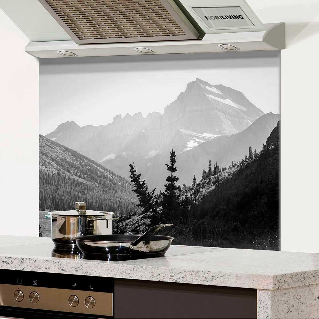 Küche mit gläsernem Spritzschutz, darauf eine schwarz-weiße Berglandschaft abgebildet. Edelstahl-Kochtopf und Pfanne auf der Arbeitsplatte.