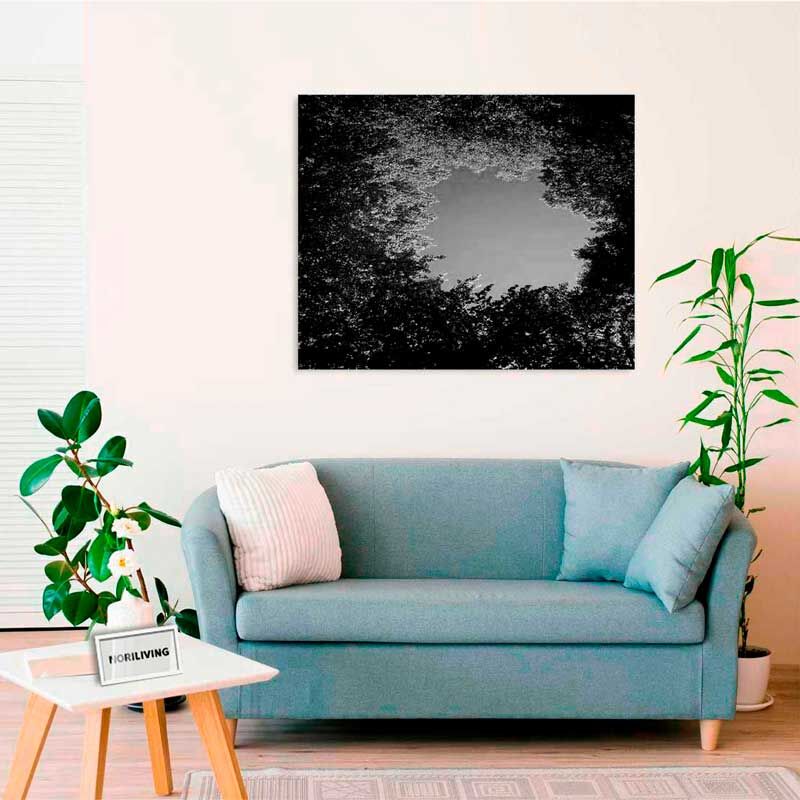 Ein helles Wohnzimmer mit einem blauen Sofa, dekorativen Kissen, einem kleinen Tisch und einem an der Wand hängenden Schwarz-Weiß-Kunstwerk mit Baumkronenmotiv.