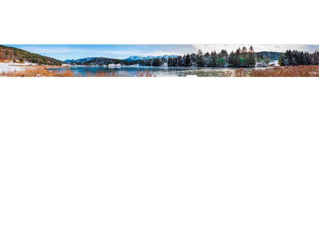 Weite Panoramaansicht eines Sees umgeben von schneebedeckten Bergen und Wald im Winter
