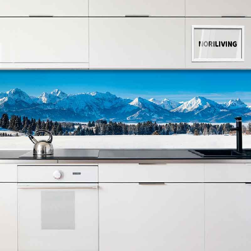 Eine moderne weiße Küche mit einer Glasrückwand, die eine malerische Alpenlandschaft zeigt.