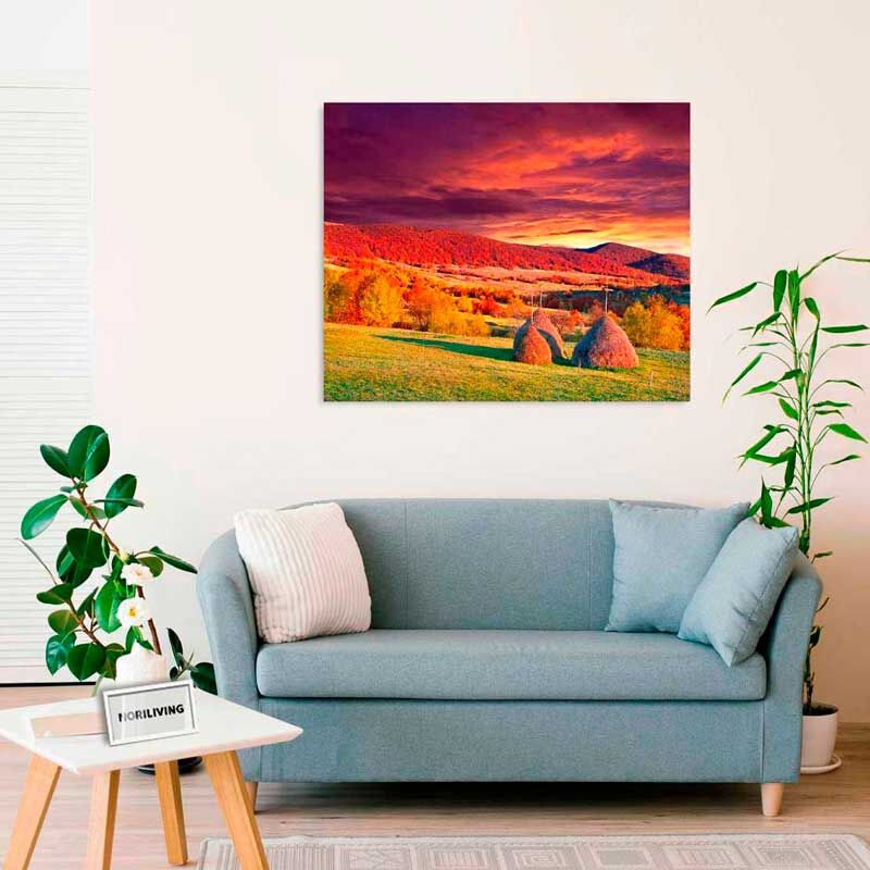 Ein Wohnzimmer mit einem blauen Sofa, Pflanzen und einem an der Wand hängenden Bild einer herbstlichen Landschaft mit dramatischem Himmel.