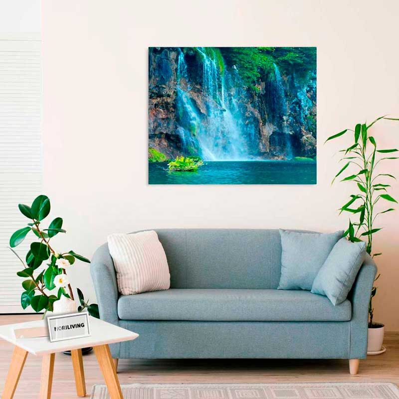 Ein Wohnzimmer mit einem grauen Sofa und einem Wasserfallbild an der Wand, umgeben von Grünpflanzen.