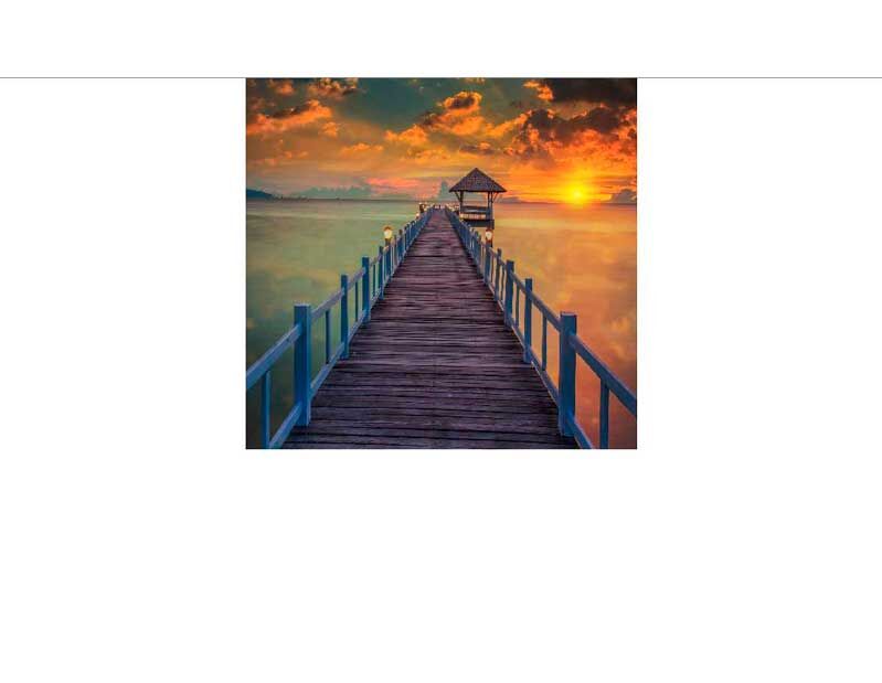 Ein langer Holzsteg führt zu einem Pavillon über dem Meer, beleuchtet von einem beeindruckenden Sonnenuntergang.