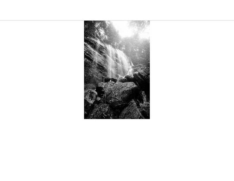 Schwarz-weißes Foto eines Wasserfalls mit Felsen im Vordergrund