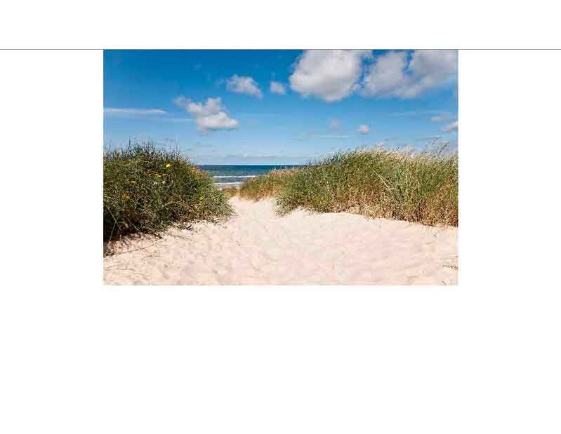 Ein sandiger Pfad führt durch die Dünen zu einem klaren blauen Meer unter einem teils wolkigen Himmel.