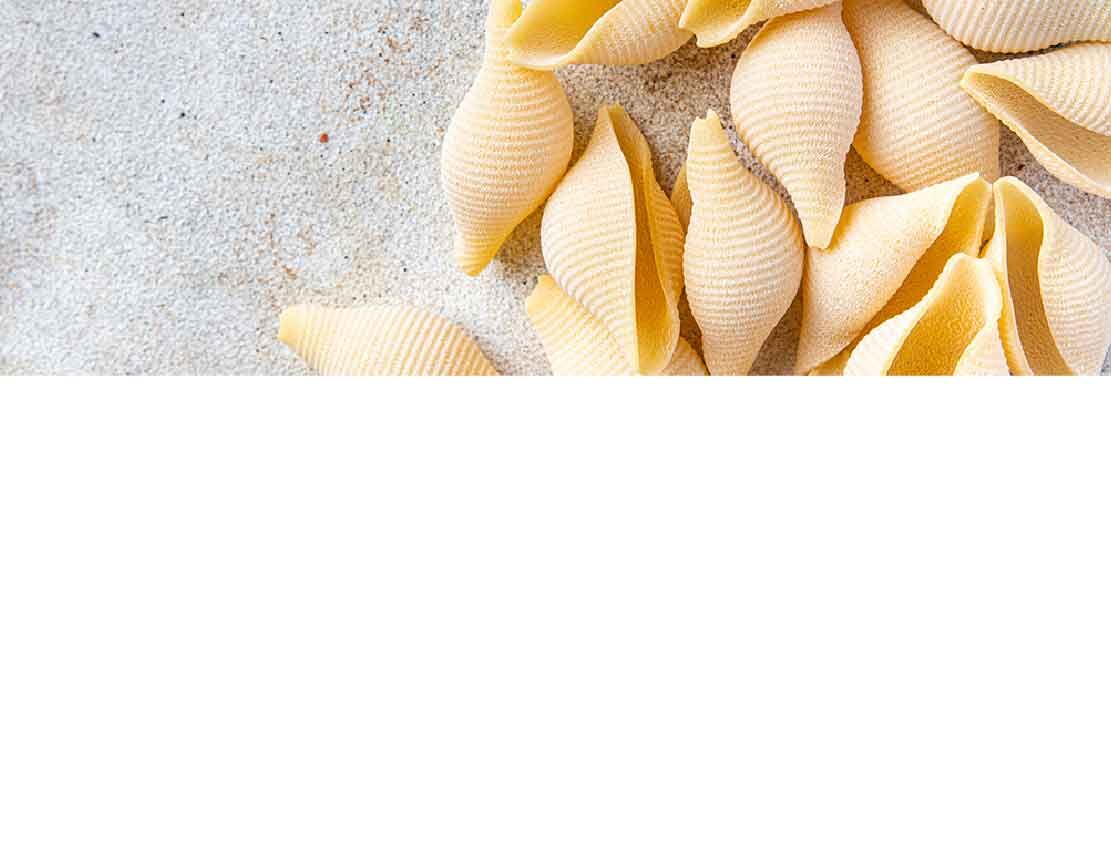 Conchiglie Nudeln aus Hartweizengrieß auf hellem Sandhintergrund liegend