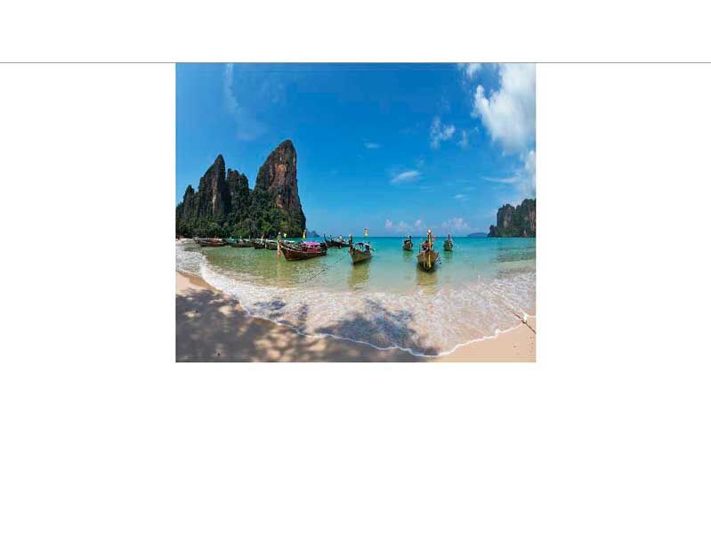 Traumhafter Strand mit sanften Wellen, Felsen im Hintergrund und traditionellen Holzbooten im türkisblauen Wasser unter strahlend blauem Himmel