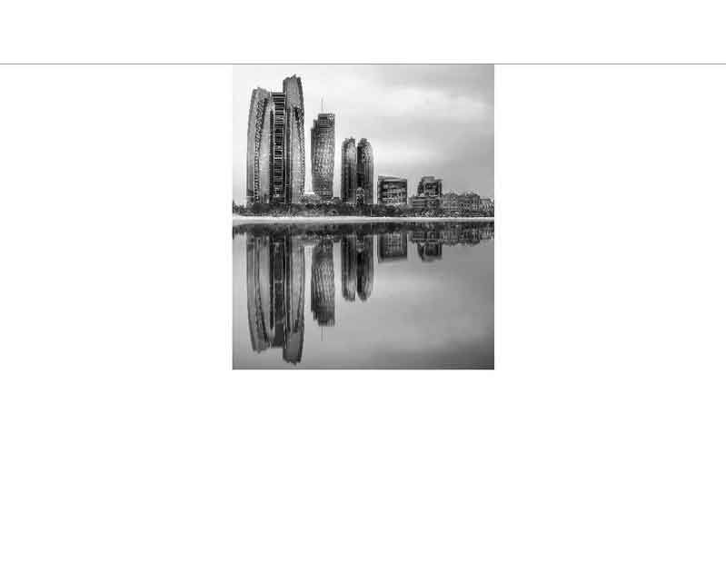 Monochromes Foto einer modernen Skyline, deren Gebäude sich im ruhigen Wasser spiegeln.