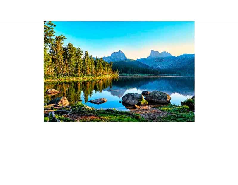 Ein idyllischer Bergsee reflektiert die umliegenden Bäume und Berge im Morgenlicht